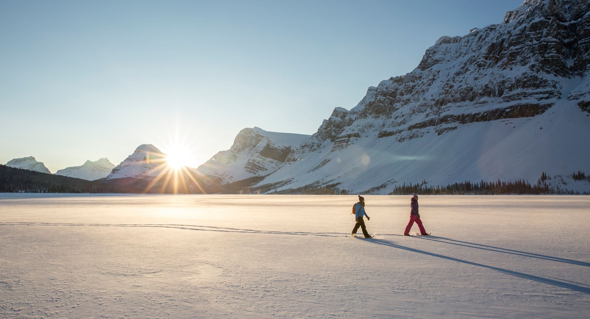 Two people snowshoeing across Bow Lake on the Icefields Parkway in the winter